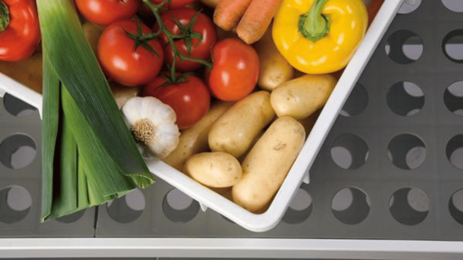 White bin filled with leeks, garlic, potatoes, tomatoes, yellow pepper, and carrots on top of FERMOD shelving