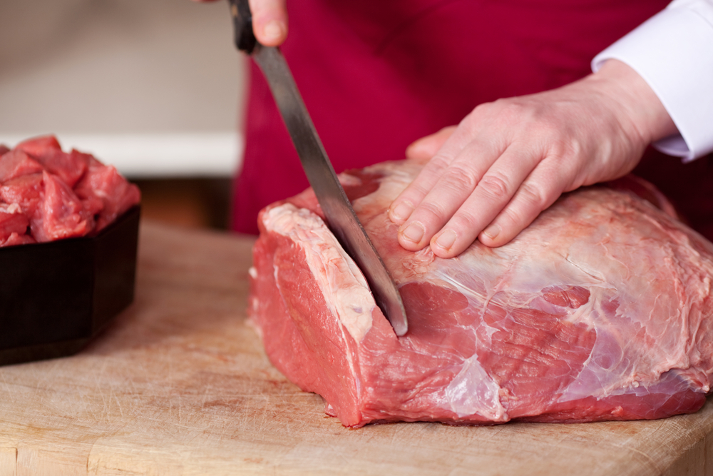 Closeup of the hands of a butcher cutting slices of raw meat off a large loin