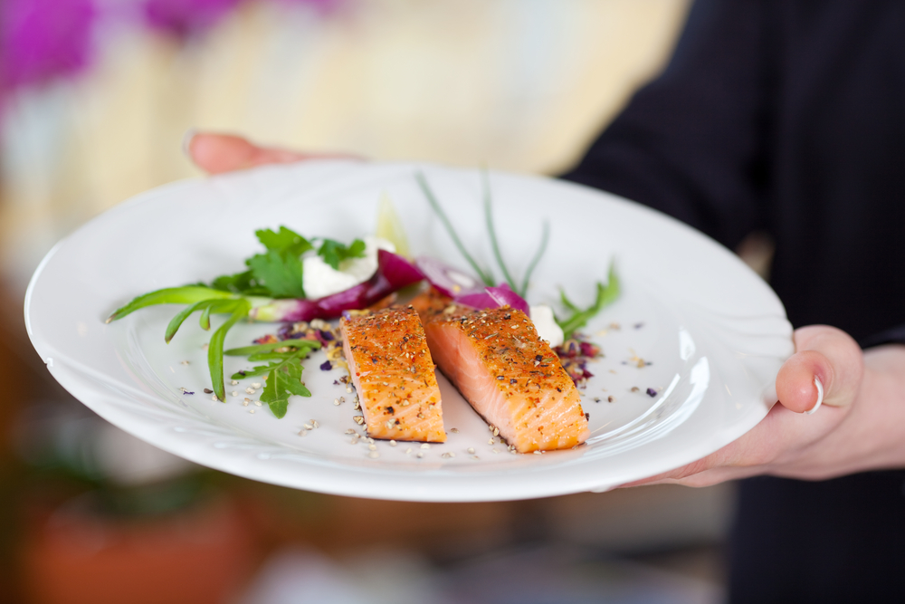Cropped image of waitress displaying salmon dish in restaurant